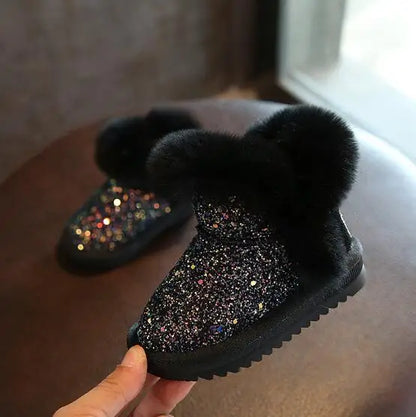 Black glittery slipper with fluffy pom-pom held by a hand on a wooden surface.