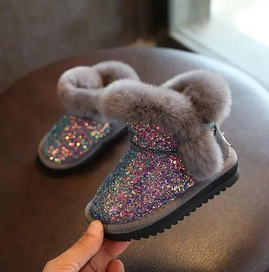 Child's glittery boot with fluffy gray top held by a hand on a wooden surface.