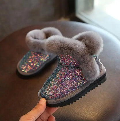 Child's glittery boot with fluffy gray top held by a hand on a wooden surface.