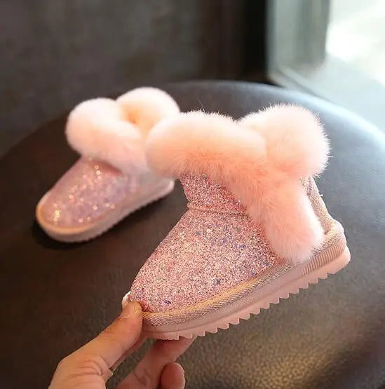 Pink glittery snow boots with fluffy tops on a dark surface