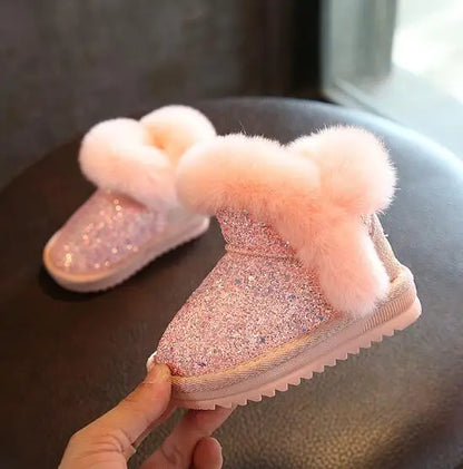 Pink glittery snow boots with fluffy tops on a dark surface